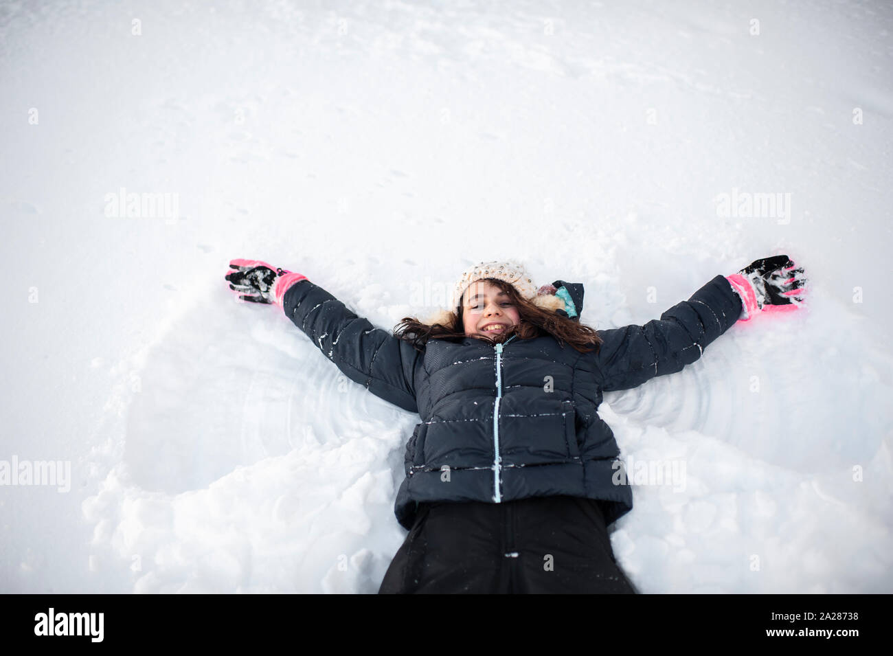 Girl smiling tout en faisant l'ange de la neige dans la neige dans la cour avant Banque D'Images