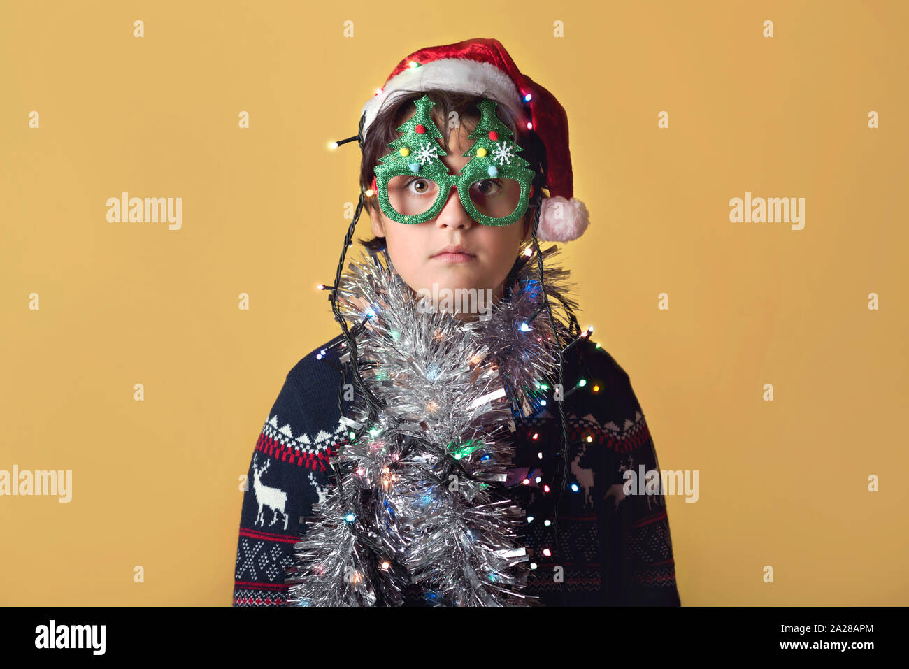 Enfant drôle avec des lumières de Noël Wearing Christmas Santa Claus Hat sur fond jaune Banque D'Images