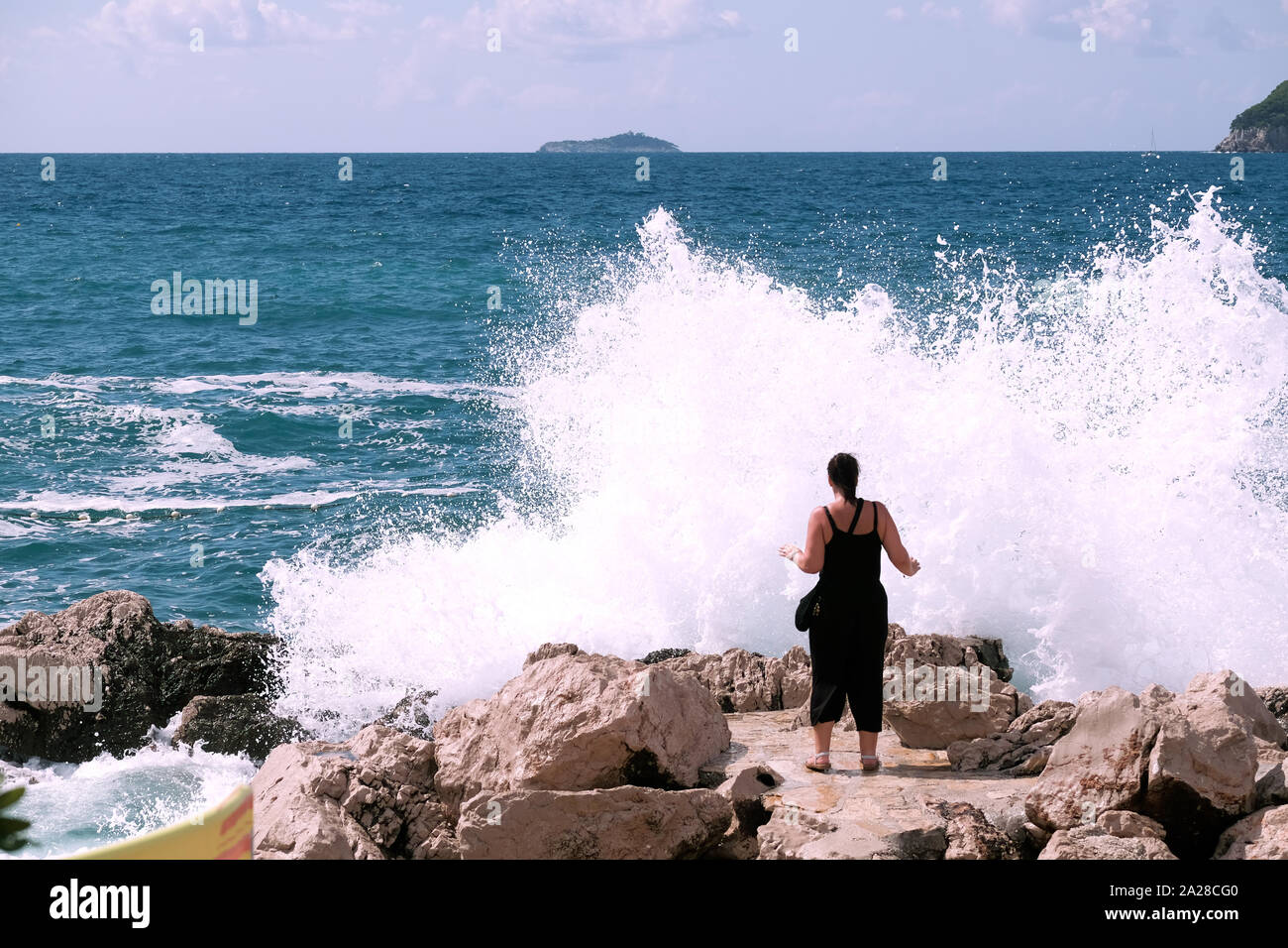 Une grande vague s'écrase dans les rochers alors qu'elle touche la terre devant un touriste à Dubrovnik, en Croatie. Un grand jet est poussé vers le haut dans l'air Banque D'Images