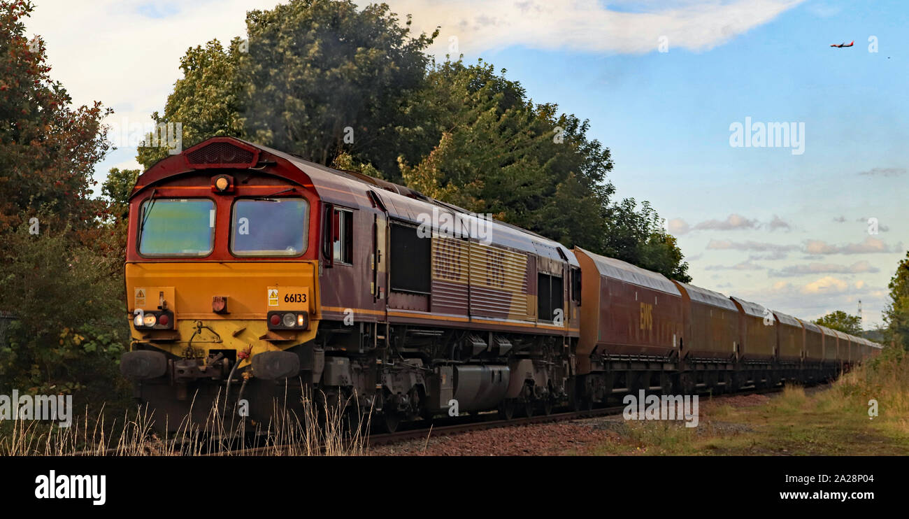 Un jaune et marron loco diesel transportant du charbon un train s'approche du passage à niveau de Holywell comme avion de ligne rend son approche de l'aéroport de Newcastle. Banque D'Images