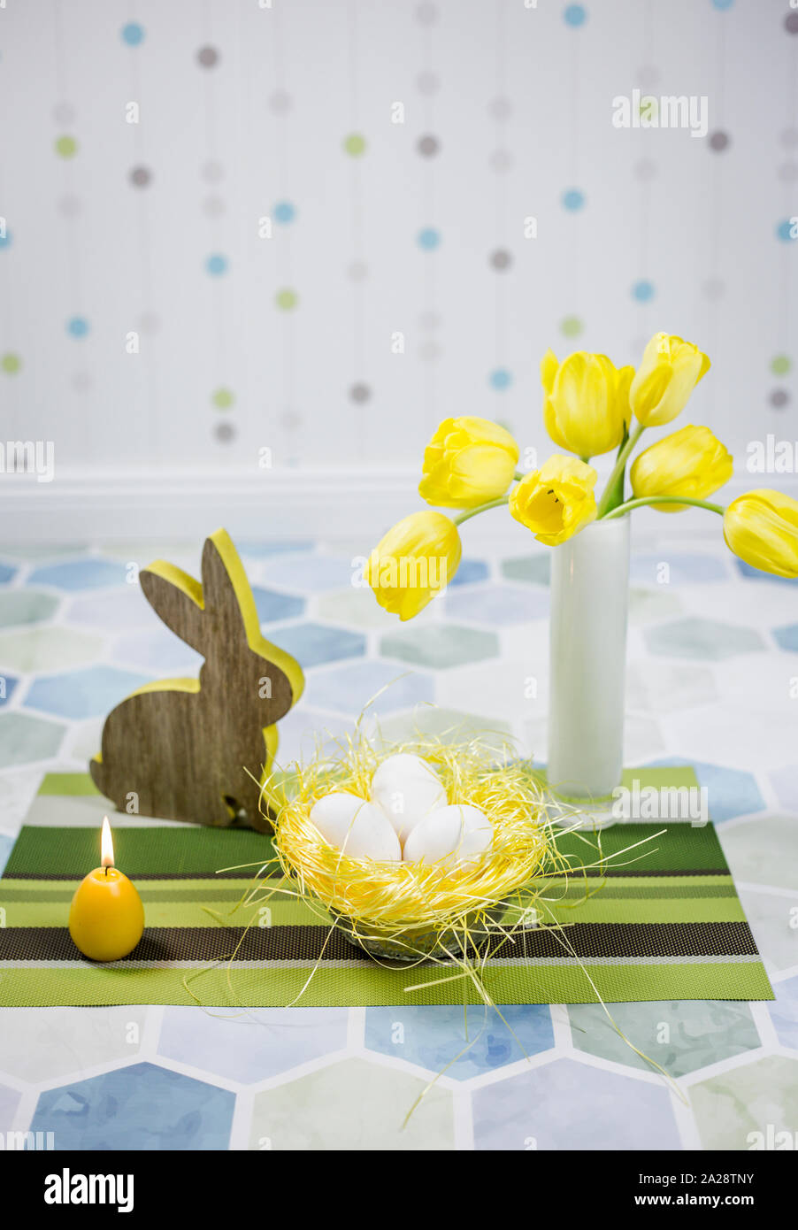 Décorations de Pâques sur une table, œufs de poulet dans un nid, tulipes jaunes dans un vase blanc. Banque D'Images