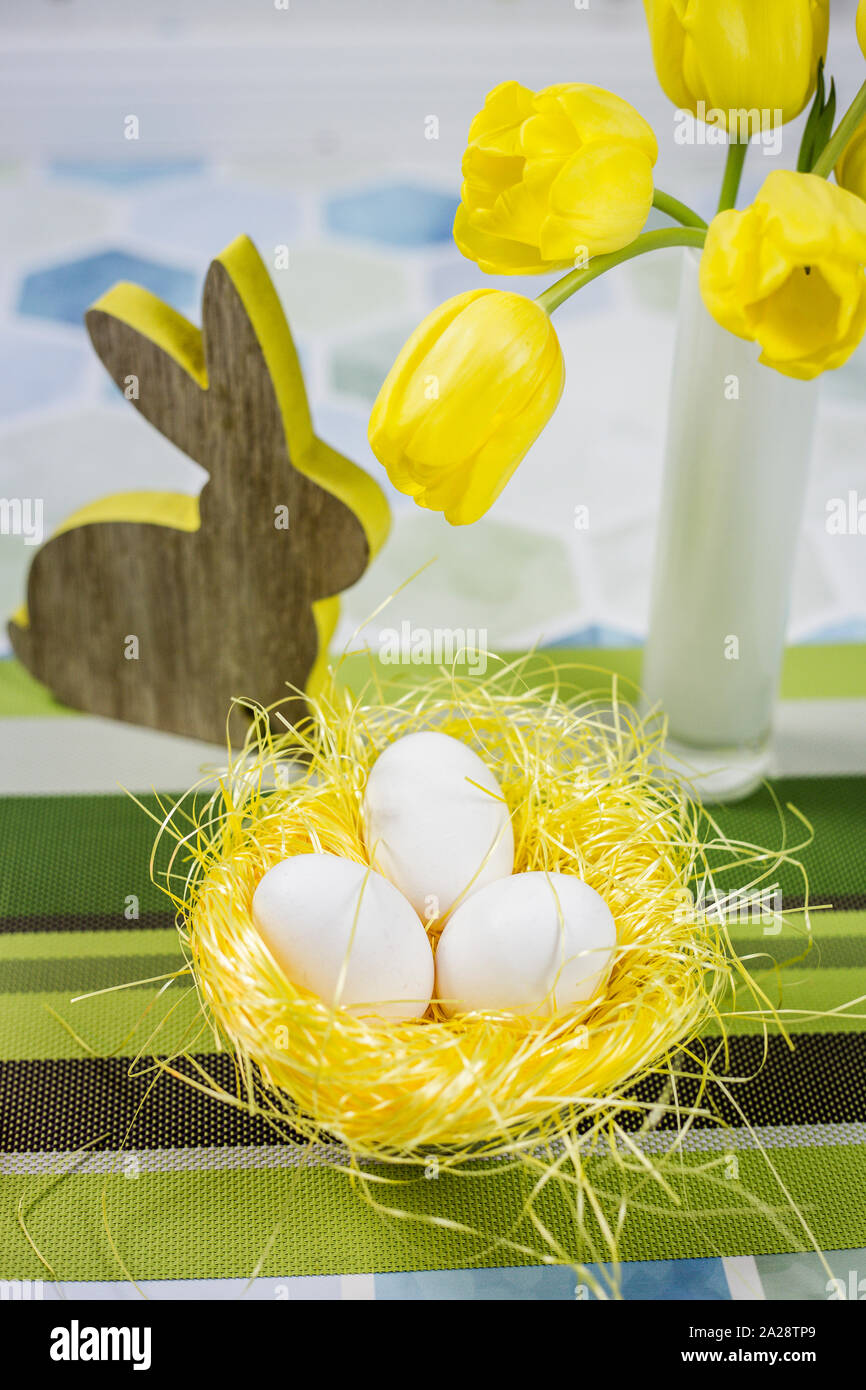 Décorations de Pâques sur une table, œufs de poulet dans un nid, tulipes jaunes dans un vase blanc. Banque D'Images