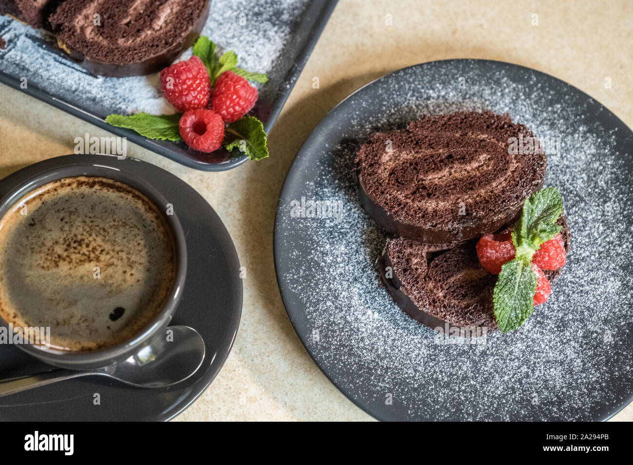 Swiss roll chocolat décoré avec des framboises sur une assiette et du café noir sur la table. Des bonbons. Focus sélectif. Banque D'Images