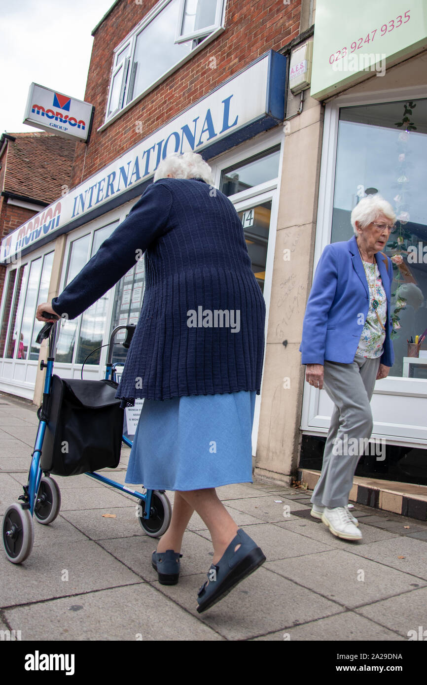 Deux femmes âgées marcher devant l'autre dans la rue, l'une des femmes est à l'aide d'un zimmer frame ou l'aide à la mobilité Banque D'Images