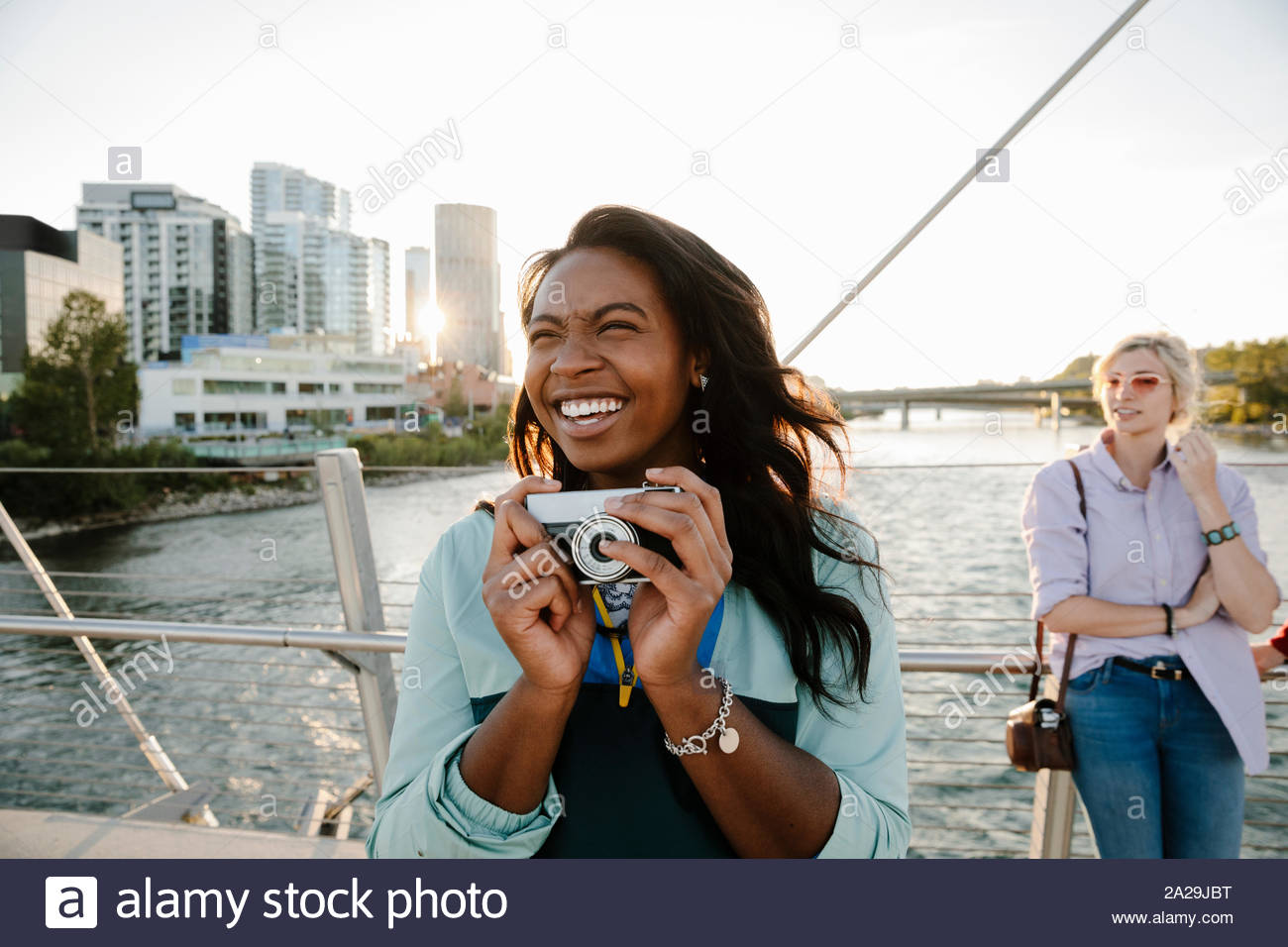 Jeune femme enjouée avec appareil photo rétro sur sunny, pont urbain Banque D'Images