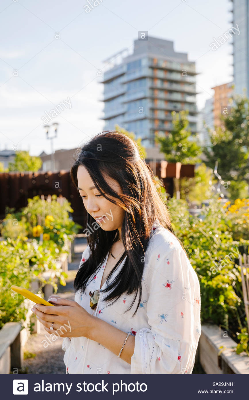 Young woman using smart phone sous le soleil, le jardin de la communauté urbaine Banque D'Images