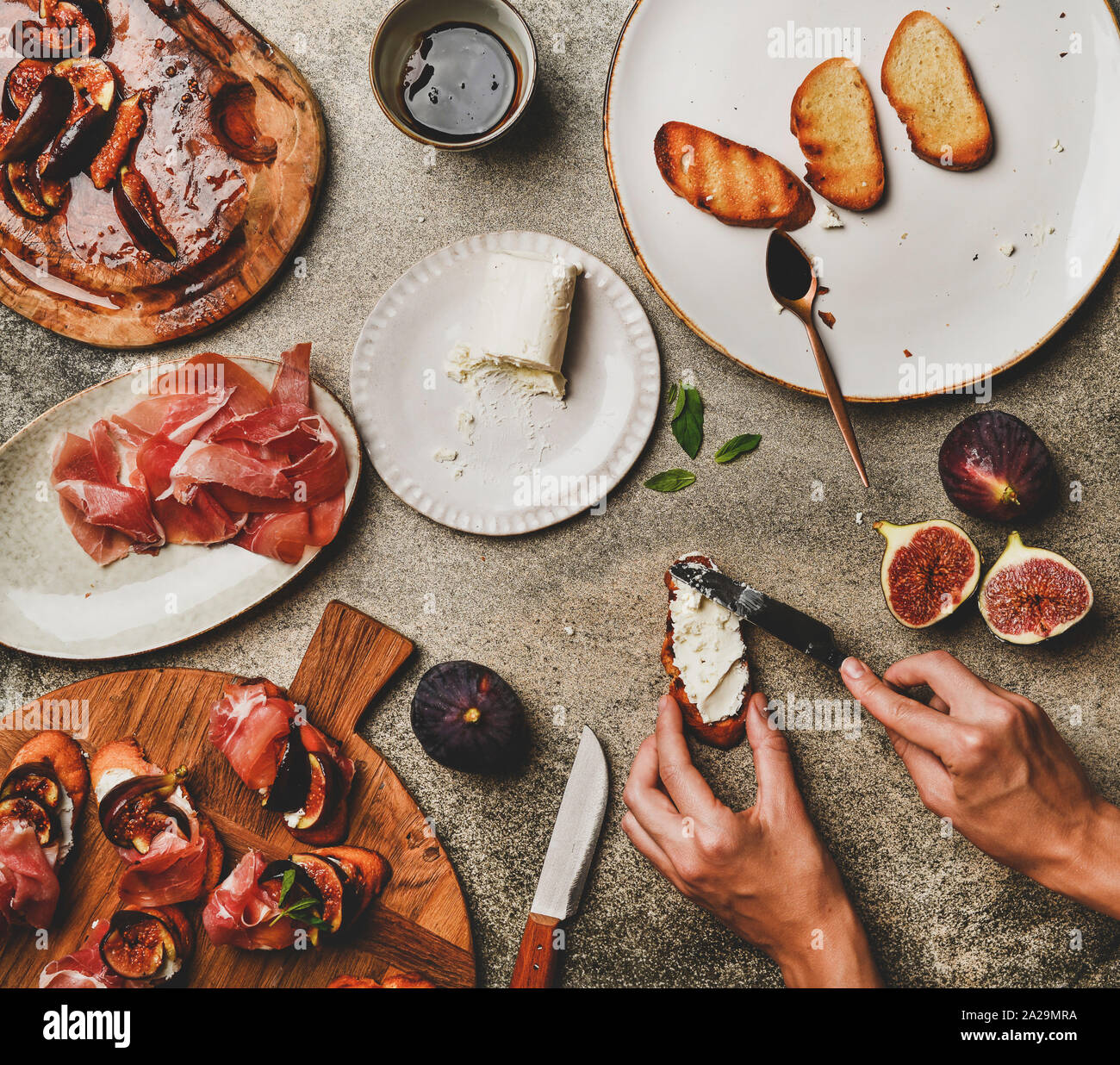 La cuisson des aliments ou de la restauration du parti. Télévision à jeter des crostini avec prosciutto, figues grillées et femelle répand les mains sur le pain de fromage de chèvre sur le béton gris Banque D'Images