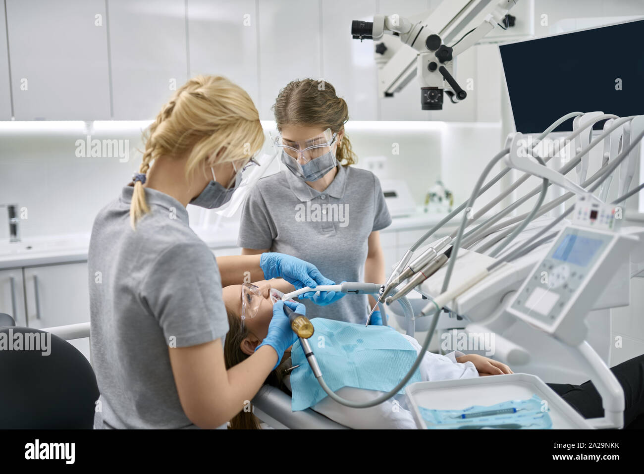 Jolie fille dans des lunettes à bretelles et d'un enrouleur joue dans une clinique dentaire. Dentiste et son assistant sont nettoyer ses dents à l'aide d'un o Banque D'Images Jolie fille dans des lunettes à bretelles et d'un enrouleur joue dans une clinique dentaire. Dentiste et son assistant sont nettoyer ses dents à l'aide d'un o Banque D'Images