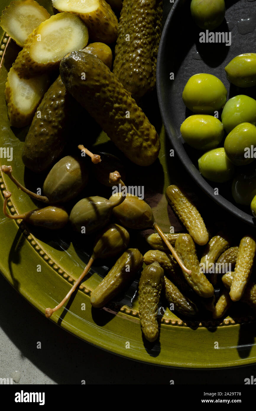 Une sélection de cornichons au vinaigre, olives vertes et câpres petits fruits sur une plaque de vert olive. Banque D'Images