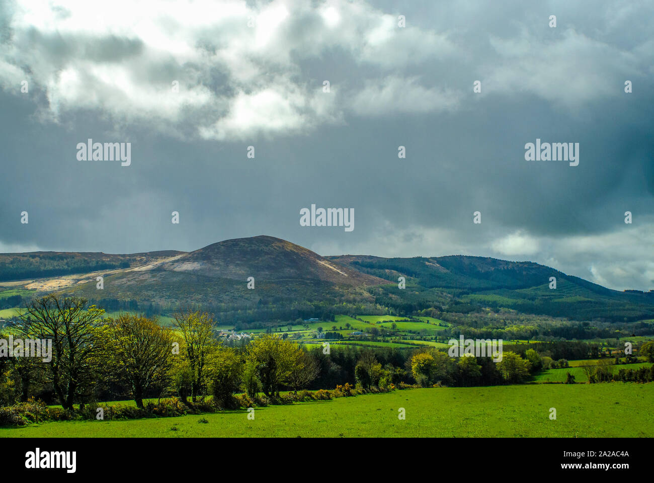 Montagne, avec green vallée fertile, avec village, nuages sombres, de diverses nuances de verts et jaunes sur les arbres. Banque D'Images