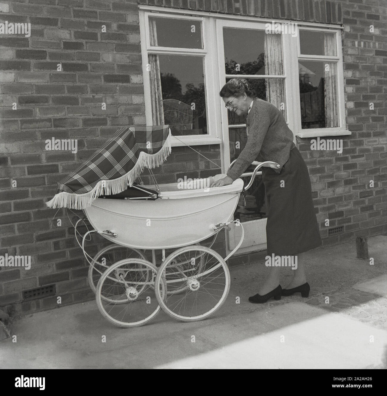 Années 1960, historique, une dame avec un landau traditionnel construit par autocar, avec couvercle de capuche en coton, sur un patio à l'extérieur d'une maison, Angleterre, Royaume-Uni. Banque D'Images