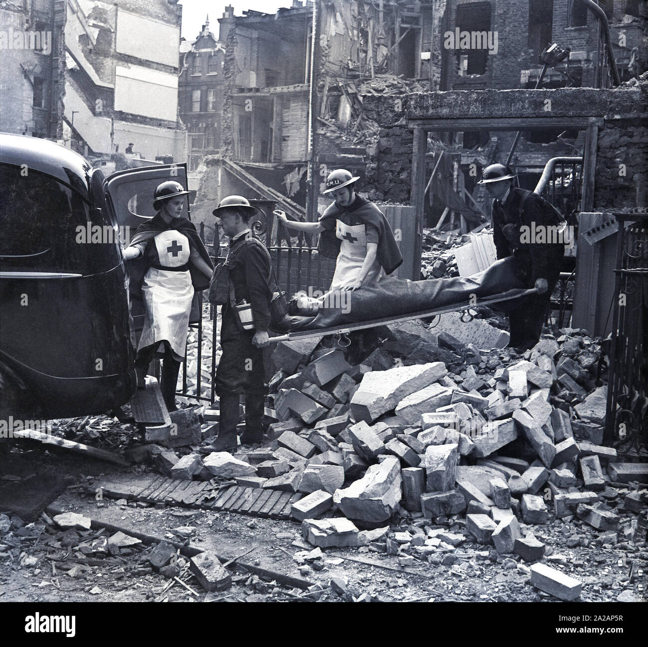 1940, historique, Londres pendant le blitz, deux gardes bénévoles masculins portant un patient civils sur une civière d'un bâtiment endommagé à la bombe à l'arrière d'un van à la suite d'un raid aérien, accompagné par les infirmières de l'UMM, PENDANT LA SECONDE GUERRE MONDIALE, en Angleterre, UK. Banque D'Images