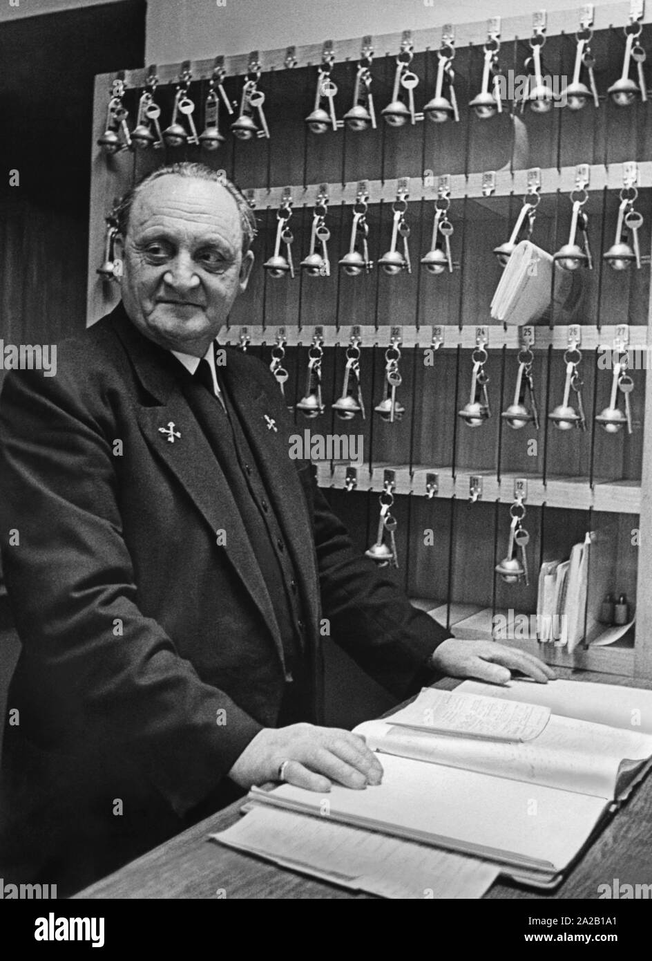 Un hôtel porter est avec l'open livre d'or à la réception d'un hôtel. La photo est probablement des années 1950. Banque D'Images