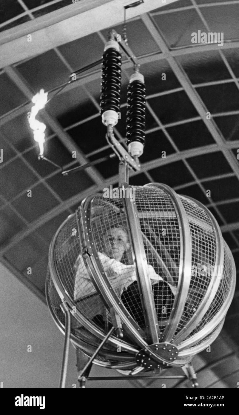 La photo montre un homme dans une cage de Faraday. Au cours de cette  présentation de l'expérience au Deutsches Museum de Munich, un fort  éclairage artificiel est déclenché, mais ne touche pas