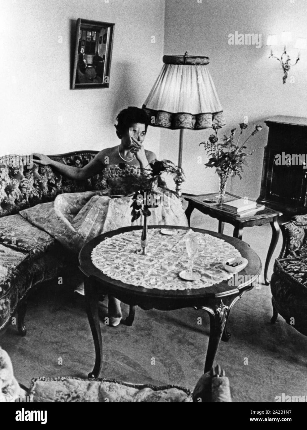Une femme est assise dans une tenue de fête sur le canapé dans un salon. Elle tient un verre de champagne dans l'air. Banque D'Images
