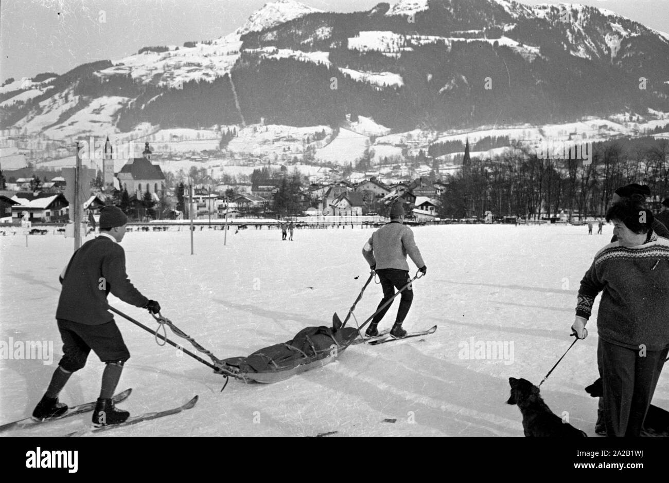 Deux membres de l'équipe de secours en montagne sur un champ de ski avec un traîneau de sauvetage. Dans l'arrière-plan sur la gauche, la ville de Kitzbuehel. La photo a été prise à l'occasion de la course du Hahnenkamm qui y ont eu lieu. La course du Hahnenkamm a eu lieu sur le Hahnenkamm de Kitzbühel depuis 1931. Banque D'Images