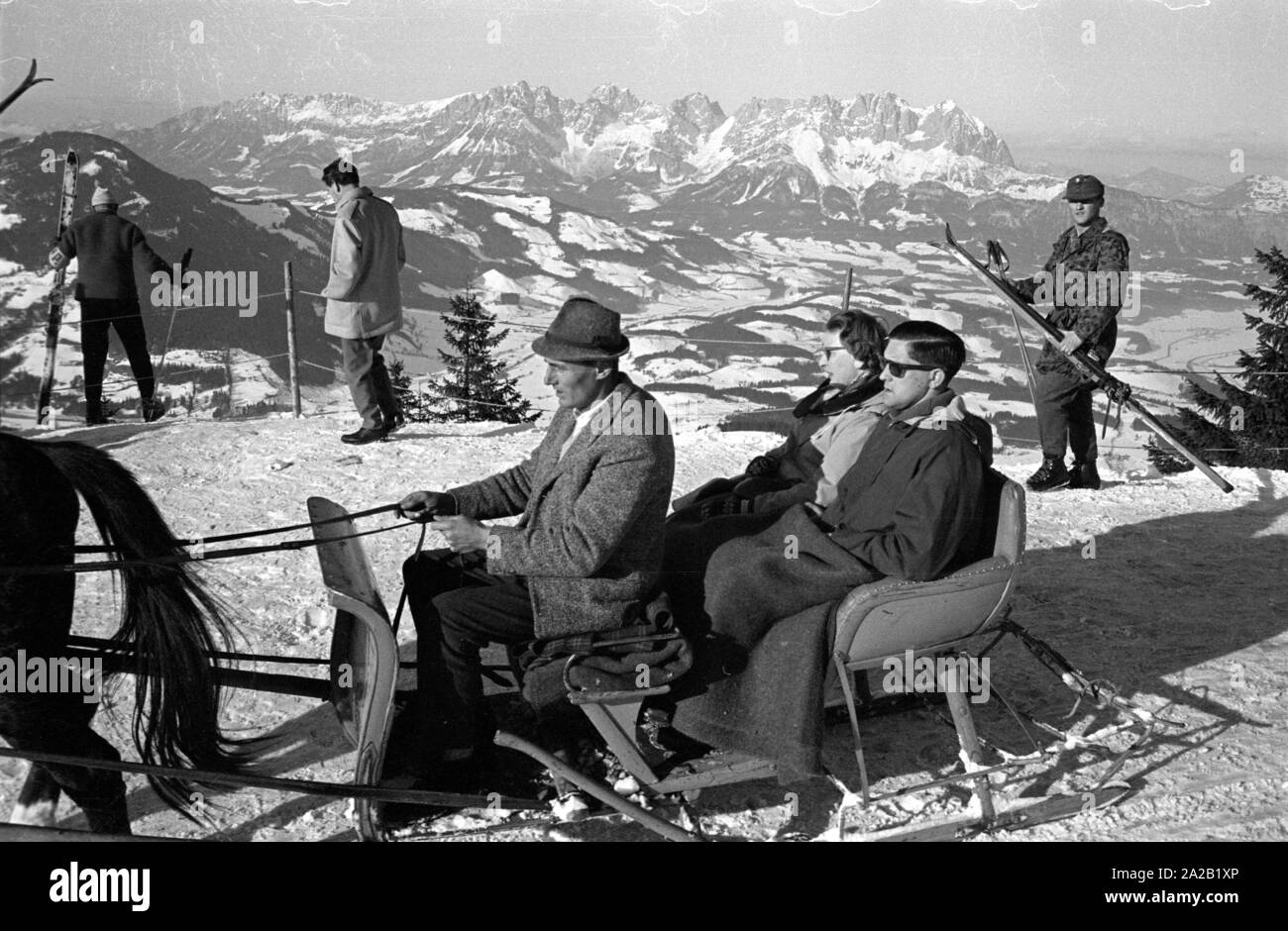 Couple sur une promenade en traîneau, certains skieurs dans l'arrière-plan et une vue sur les Alpes. La photo a été prise à l'occasion de la course du Hahnenkamm en 1962. La course du Hahnenkamm a eu lieu sur le Hahnenkamm de Kitzbühel depuis 1931. Banque D'Images