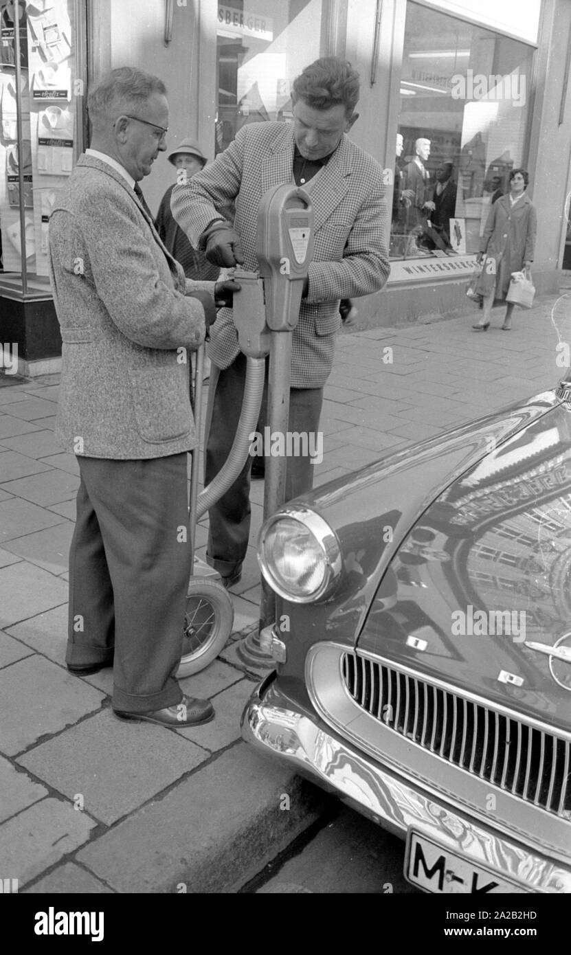 Deux fonctionnaires de vider les parcomètres installés dans le centre-ville de Munich. Après l'ouverture du parking meter les pièces tombent dans le petit coffre-fort mobile, grâce à une sorte de tuyau en plastique. L'ensemble de la construction n'est pas sans rappeler un sac chariot. Les parcomètres était de plus en plus souvent mis en place à Munich pour l'interdiction des parkers à long terme du centre-ville depuis le milieu des années 1950. Photo de fonctionnaires vidange d'un parcomètre. Banque D'Images