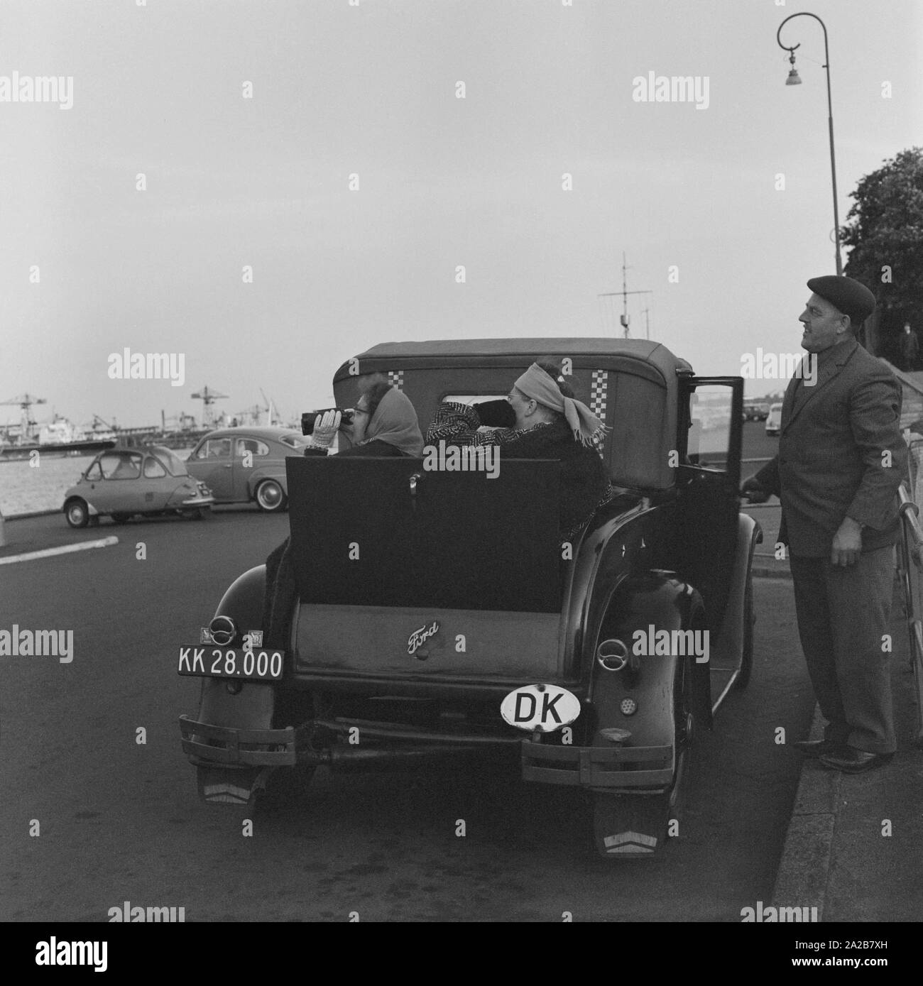 Deux femmes avec des jumelles dans le siège d'urgence d'une Ford Modèle C40 avec la plaque d'immatriculation danoise, regarder les navires dans un port. Dans l'arrière-plan un Heinkel kabine (avant) et d'une Volvo PV444 L ('Buckelvolvo'). Banque D'Images