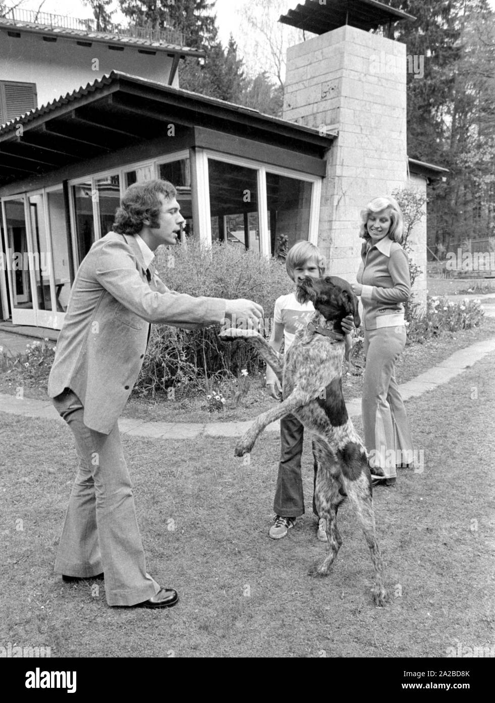 Accueil Histoire avec la famille Beckenbauer. Dans la photo : Franz Beckenbauer (l.), jouant dans le jardin avec le chien. Droit dans l'image, sa femme Brigitte Beckenbauer. Légèrement dissimulé, fils Thomas. Banque D'Images