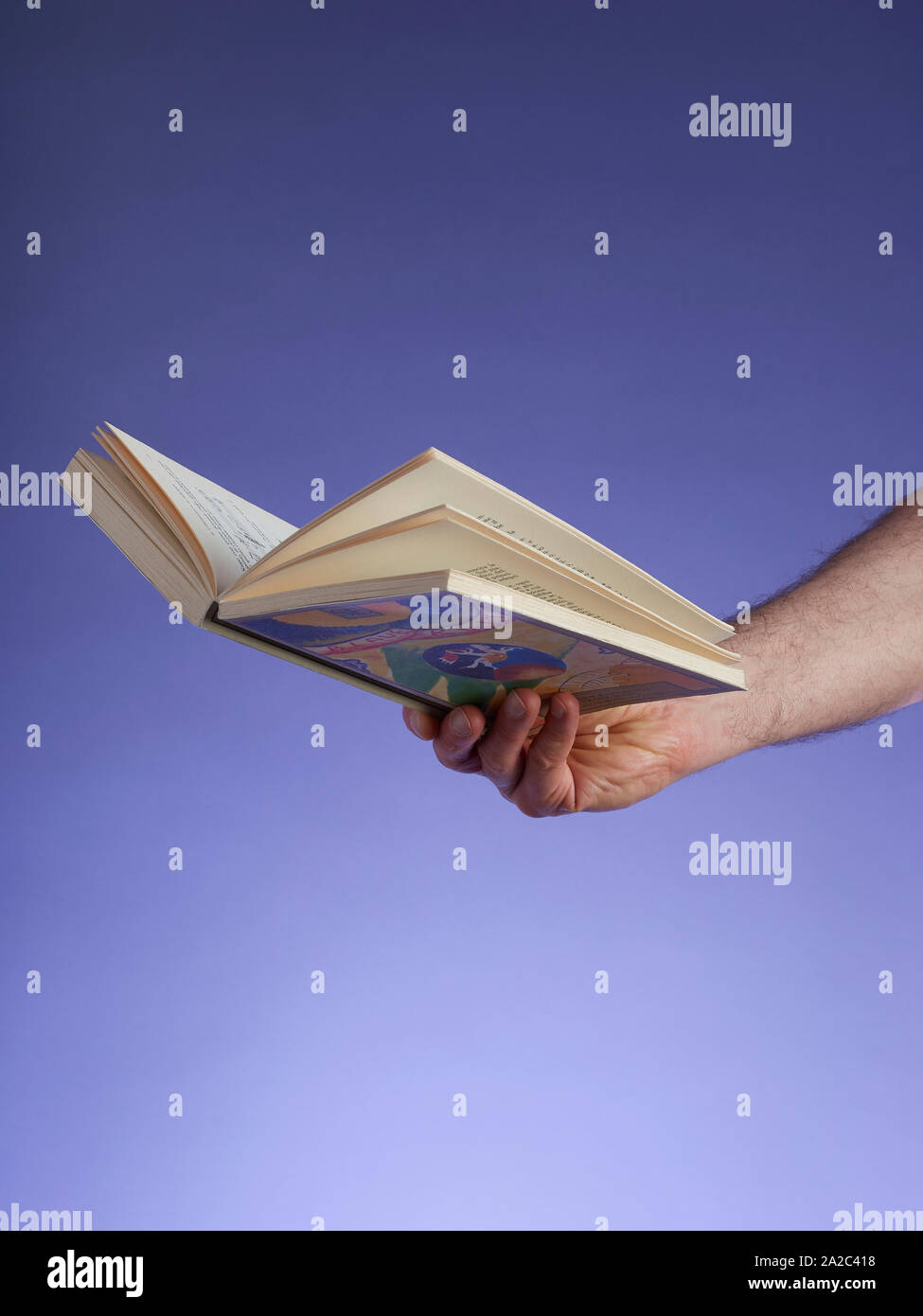 Un livre ouvert de non-fiction, tenue par un homme de main d'entrer par le côté droit, sur un fond dégradé violet-bleu Banque D'Images