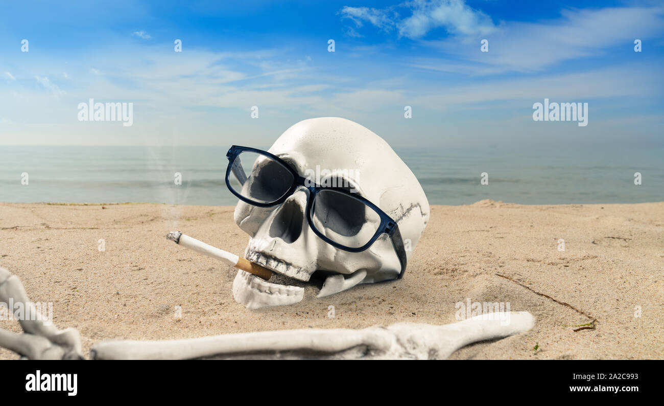 Concept de la dépendance de la cigarette un squelette avec une cigarette se trouve dans le sable Banque D'Images
