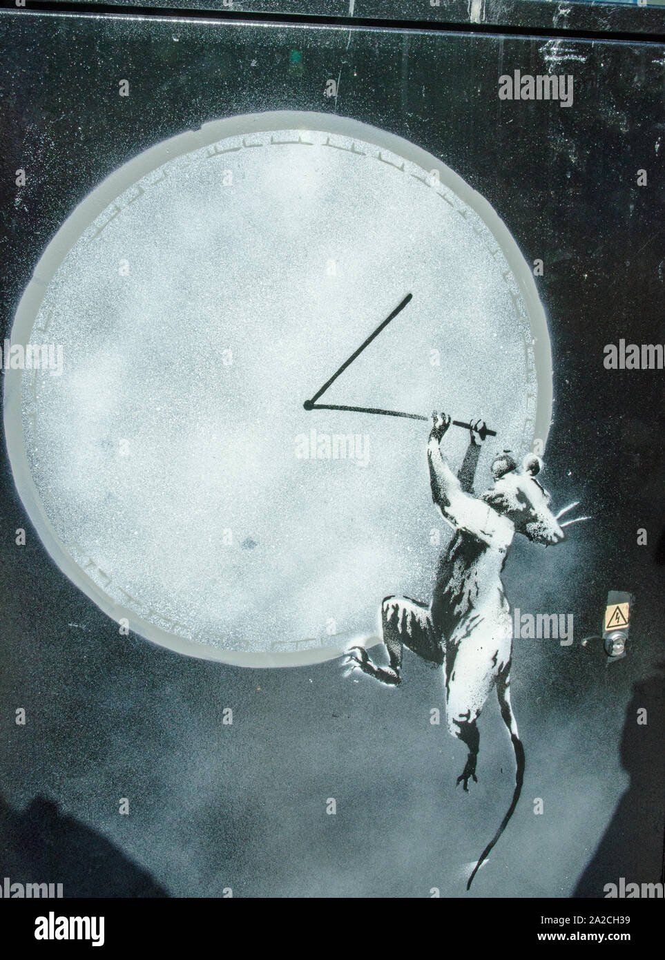 Pochoir de Banksy, un rat s'accrocher aux mains d'une horloge. Pulvérisée sur une pièce de mobilier urbain sur un trottoir à Croydon, dans le sud de Londres. Banque D'Images