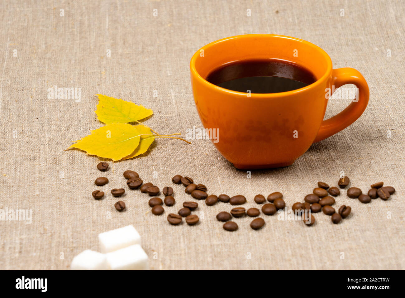 Une tasse de café noir chaud, tombée des feuilles jaunes et les grains de café à côté d'un tissu d'arrière-plan. Thème de l'automne. Banque D'Images