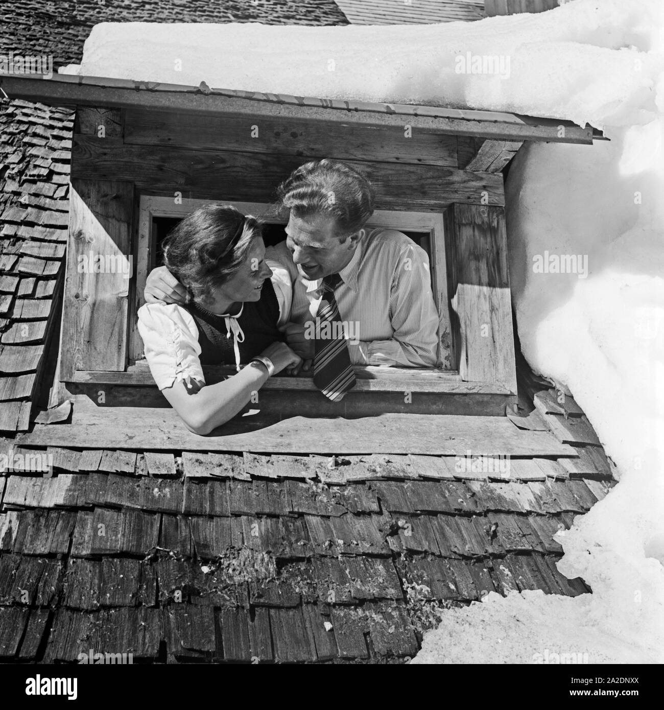 Ein junges Paar schaut aus einem verschneiten Dachfenster, Deutschland 1930 er Jahre. Un jeune couple à une fenêtre de toit dans la neige, l'Allemagne des années 1930. Banque D'Images
