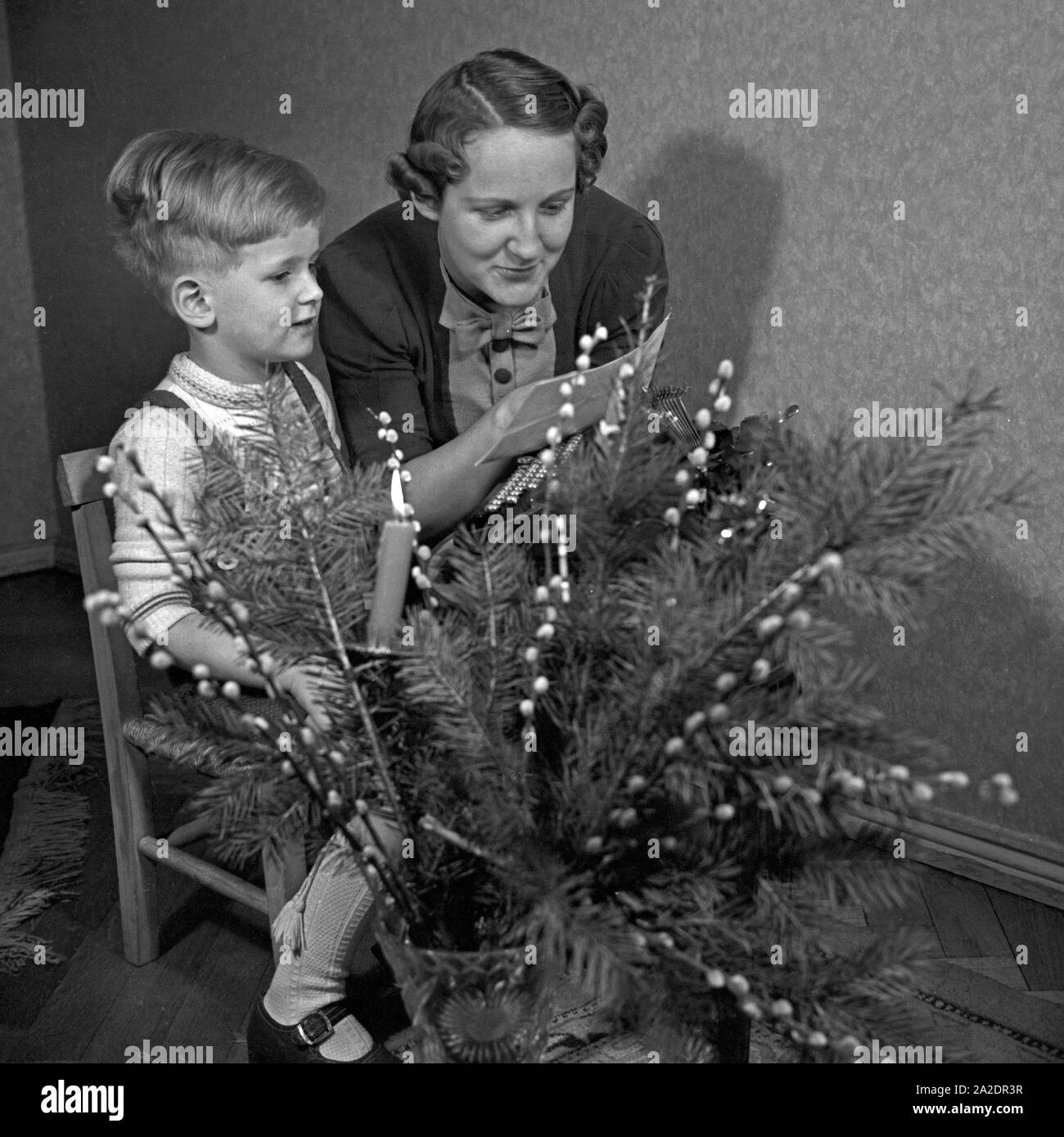 Ein kleiner Junge schreibt seinen Wunschzettel an den Weihnachtsmann mit der Schreibmaschine und gibt ihn senneur Mutter zur Weiterleitung, Deutschland 1930 er Jahre. Un petit garçon tapant sa liste de souhaits et lui donne sa mère pour transmission à Santa, Allemagne 1930. Banque D'Images