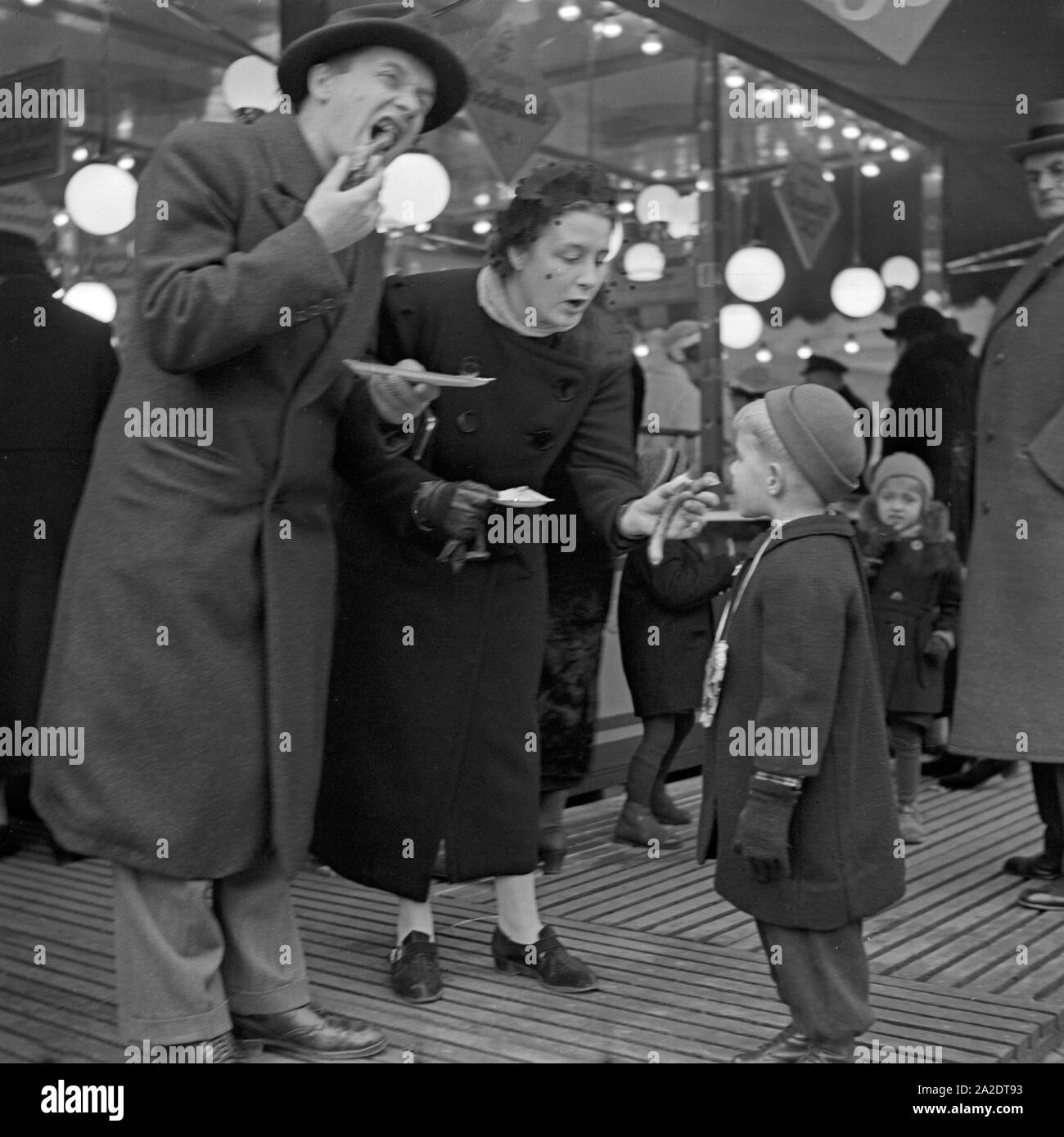 Die Eltern mit ihrem kleinen Jungen vor der Wurstbraterei Würstchen Essen und auf dem Weihnachtsmarkt Deutschland, 1930er Jahre. Les parents et leur petit garçon en face d'un snack-bar stand lors du marché de noël de manger des saucisses, Allemagne 1930. Banque D'Images