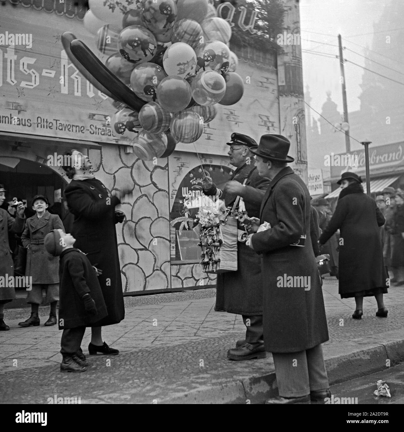 Ein kleiner Junge steht nur Luftballonverkäufer senneur Mutter Haus am Eingang des Weihnachtsmarkt Deutschland, 1930 er Jahre. Un petit garçon avec sa mère debout par un vendeur de ballon à l'entrée du marché de noël, Allemagne 1930. Banque D'Images