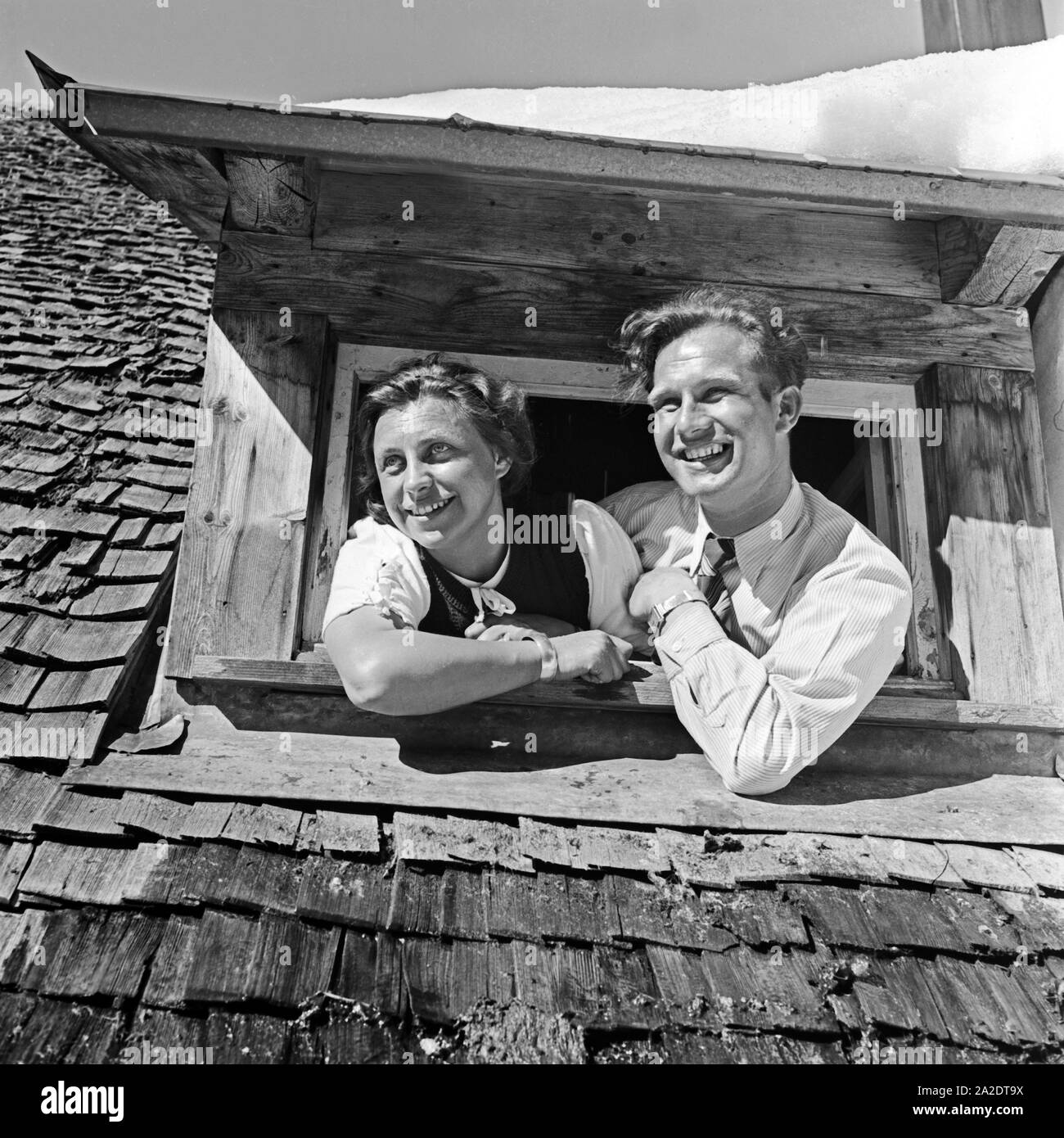 Ein junges Paar schaut aus einem verschneiten Dachfenster, Deutschland 1930 er Jahre. Un jeune couple à une fenêtre de toit dans la neige, l'Allemagne des années 1930. Banque D'Images
