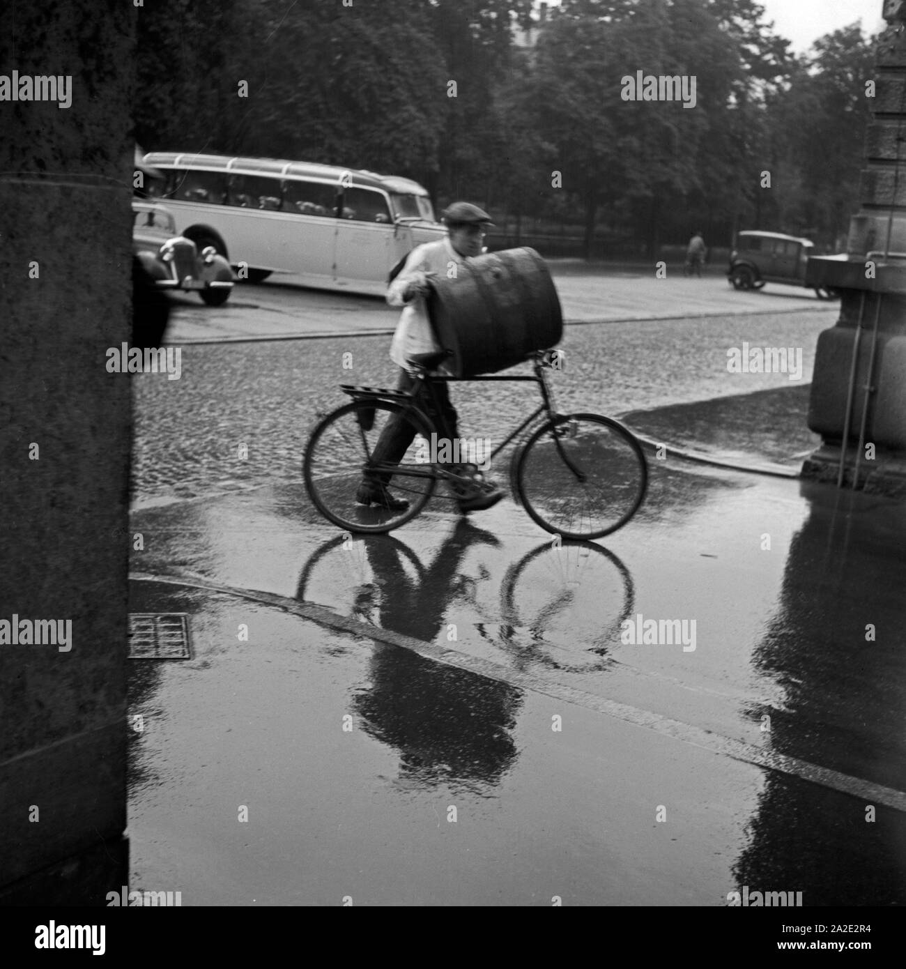 Ein Mann einFas transportiert auf seinem Fahrrad durch den Regen, Deutschland 1930er Jahre. Un homme transportant un canon sur son vélo à travers la pluie, Allemagne 1930. Banque D'Images
