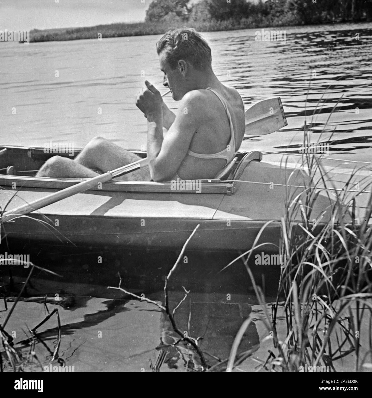 Ein Mann zündet sich in seinem Klepper Faltboot im Schilf entspannt eine Zigarette un, Deutschland 1930 er Jahre. Un homme allumer une cigarette dans son pliant Klepper bateau sur un lac, l'Allemagne des années 1930. Banque D'Images
