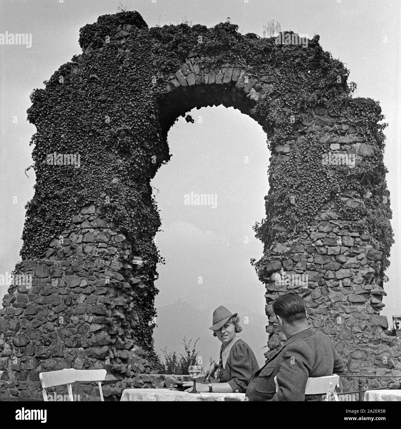 Ein Paar sitzt auf einer Terrasse vor dem Rolandsbogen dans Rolandswerth, einem Stadtteil von Remagen, Deutschland 1930 er Jahre. Un couple assis sur une terrasse de restaurant en face de l'arche à Rolandsbogen Rolandswerth près de Remagen, Allemagne 1930. Banque D'Images