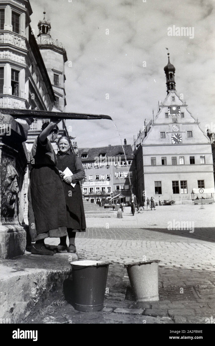 Zwei Frauen verwalten sich während Sie die Wassereimer mit Wasser aus dem Springbrunnen Am Marktplatz vor dem Rathaus und der Ratstrinkstube voll laufen lassen, Rothenburg ob der Tauber, Allemagne Allemagne Années 1930 er Jahre. Deux femmes ayant un chat tandis que le bucktes sont remplissage avec de l'eau de la fontaine sur la place du marché à proximité de la mairie et Ratstrinkstube à Rothenburg ob der Tauber, Allemagne 1930. Banque D'Images