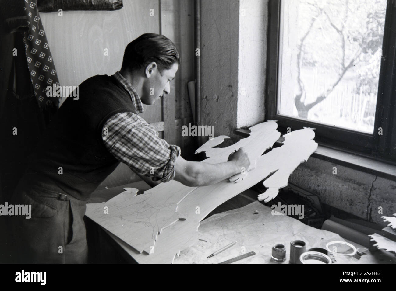 Ein Mitarbeiter in den Heller Kunst Werkstätten in der Eifel zeichnet das Motiv von ausgesägten Holzfigur zum Bemalen späteren vor, Deutschland 1930 er Jahre. Un employé de la Heller Kunst des ateliers dans l'Eifel dimensions le motif sur une figure en bois, sciés, Allemagne 1930. Banque D'Images