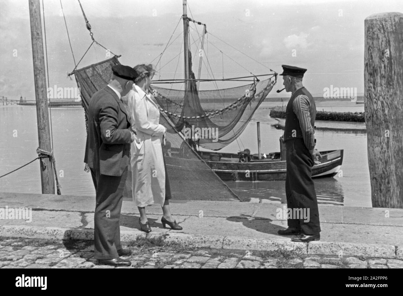 Eine Frau und ein Mann treffen einen Fischer Fischerboot vor seinem à Norddeich, Deutschland 1930 er Jahre. Une femme et un homme rencontre un pêcheur en face de son bateau à Norden, Allemagne 1930. Banque D'Images