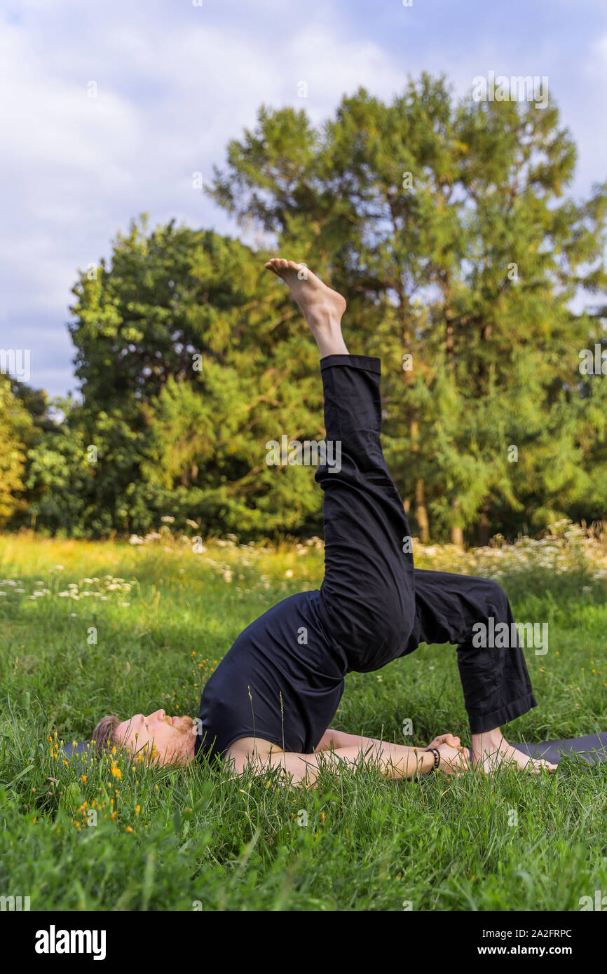 Inspiré man doing yoga asanas dans city park. L'extérieur de remise en forme et vie personnelle concept. Stretching Banque D'Images