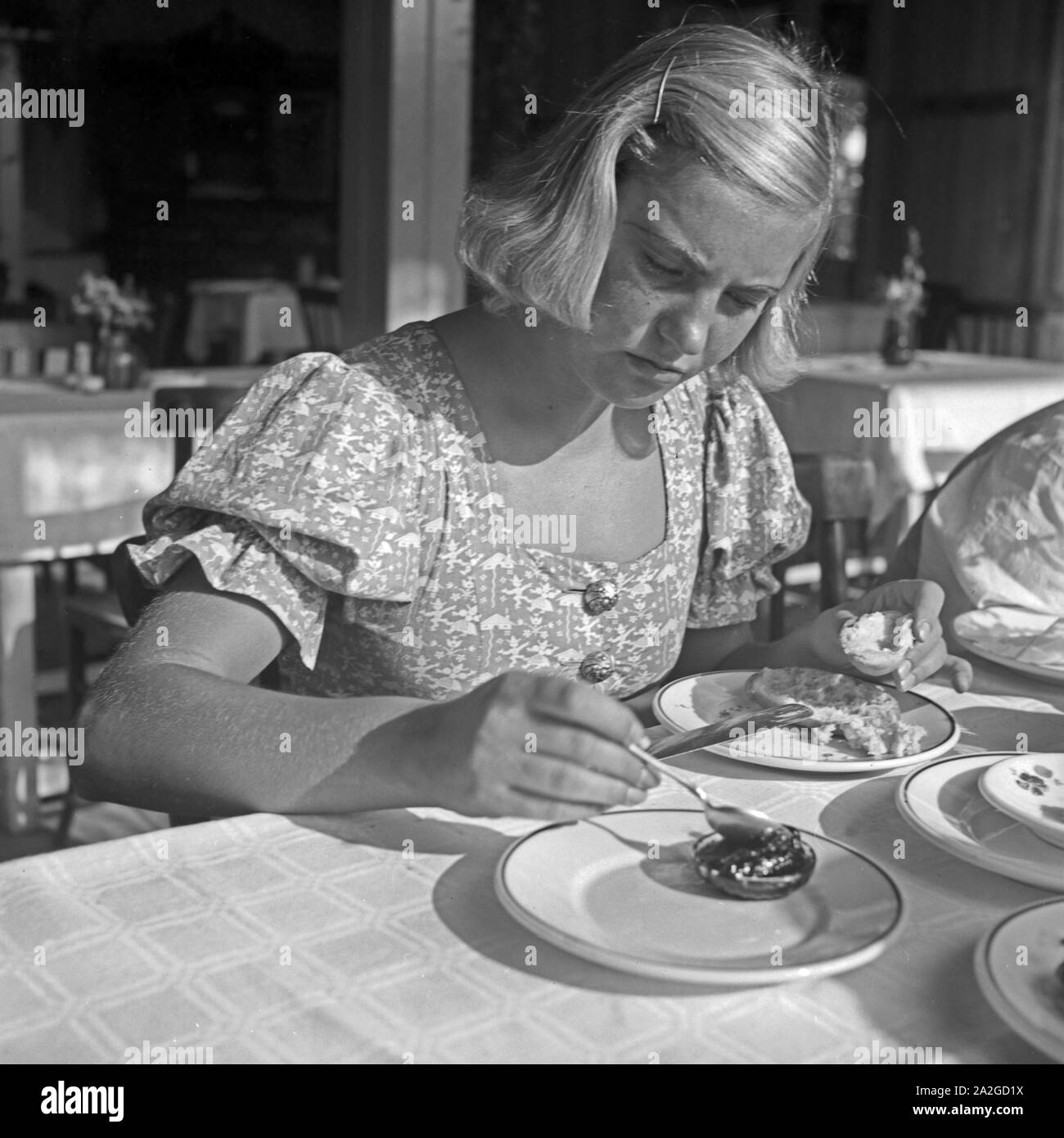 Eine junge Frau nimmt ein Brötchen zum Frühstück mit Marmelade, 1930er Jahre. Une jeune femme ayant un rouleau avec de la confiture pour le petit déjeuner, 1930. Banque D'Images