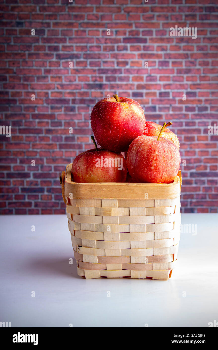 Pommes sur un panier en bois sur un tableau blanc avec un mur de briques Banque D'Images