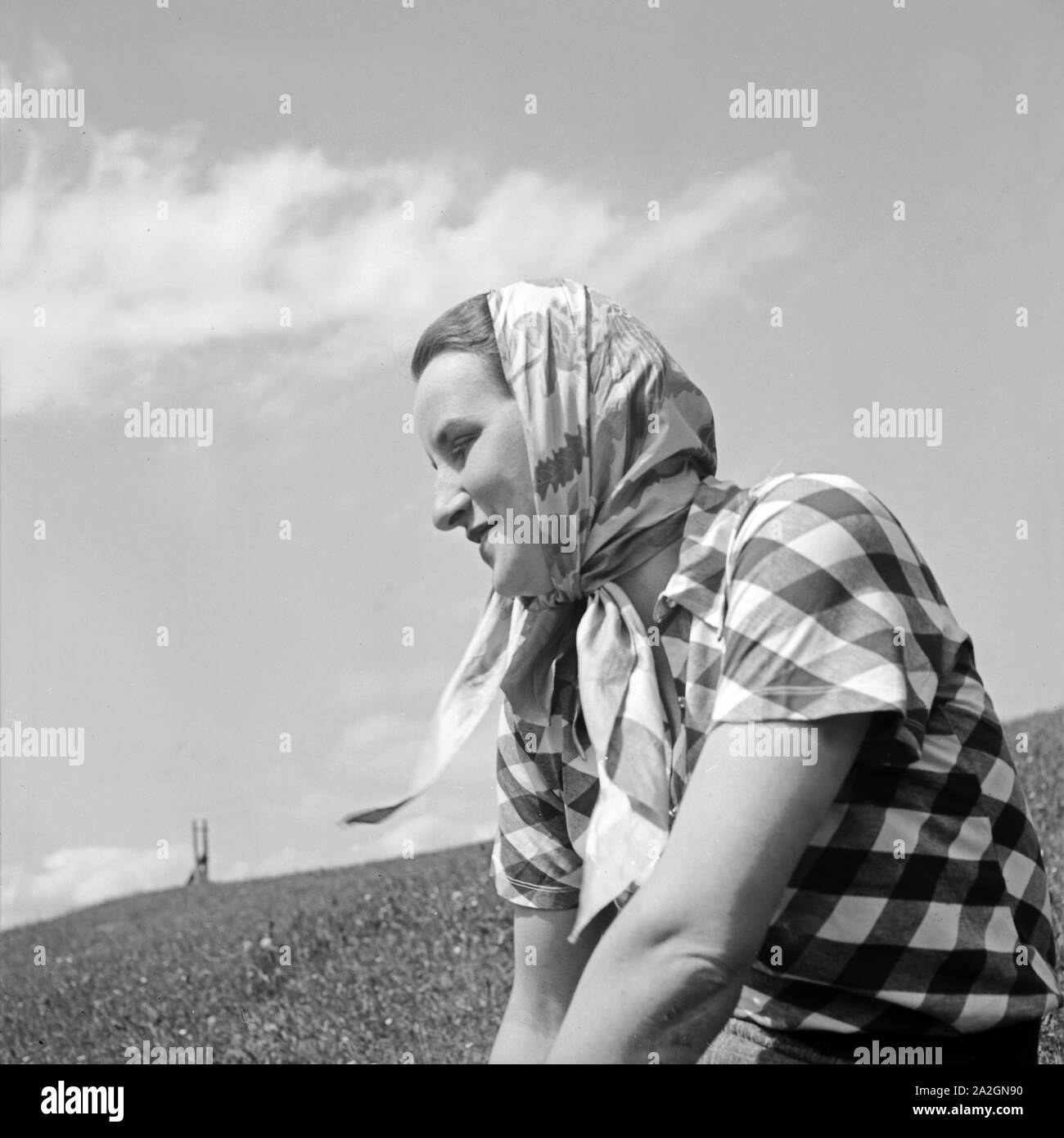 Eine junge Frau mit Kopftuch sitzt auf einer Wiese, Deutschland 1930 er Jahre. Une jeune femme avec un foulard assis dans une pelouse, Allemagne 1930. Banque D'Images