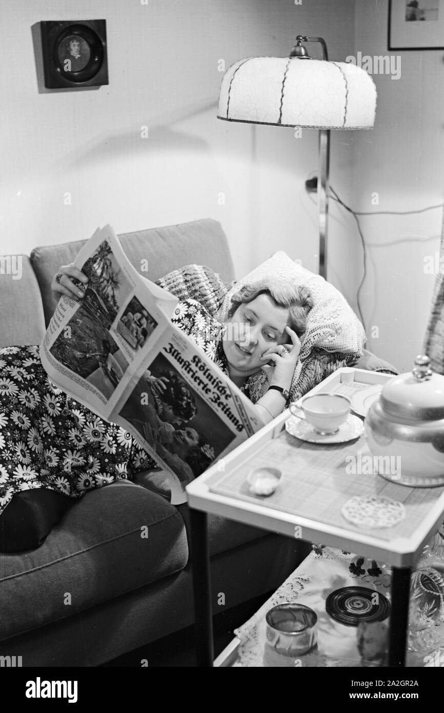 Eine Frau liegt auf dem canapé und liest die Kölnische Illustrierte Zeitung, Deutschland 1930 er Jahre. Une femme sur le canapé de la lecture du "Koelnische Illustrierte Zeitung' Journal, Allemagne 1930. Banque D'Images