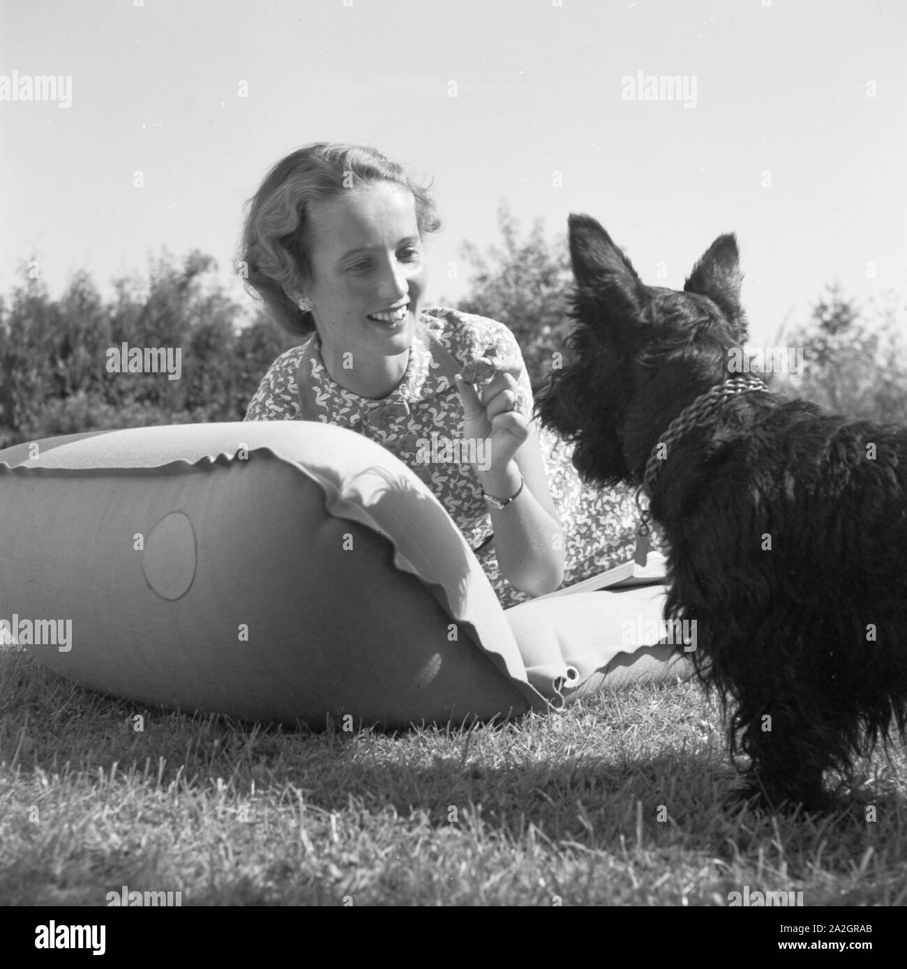 Eine junge Frau mit ihrem Hund auf einer Wiese, Deutschland 1930 er Jahre. Une jeune femme avec son chien sur une pelouse, Allemagne 1930. Banque D'Images