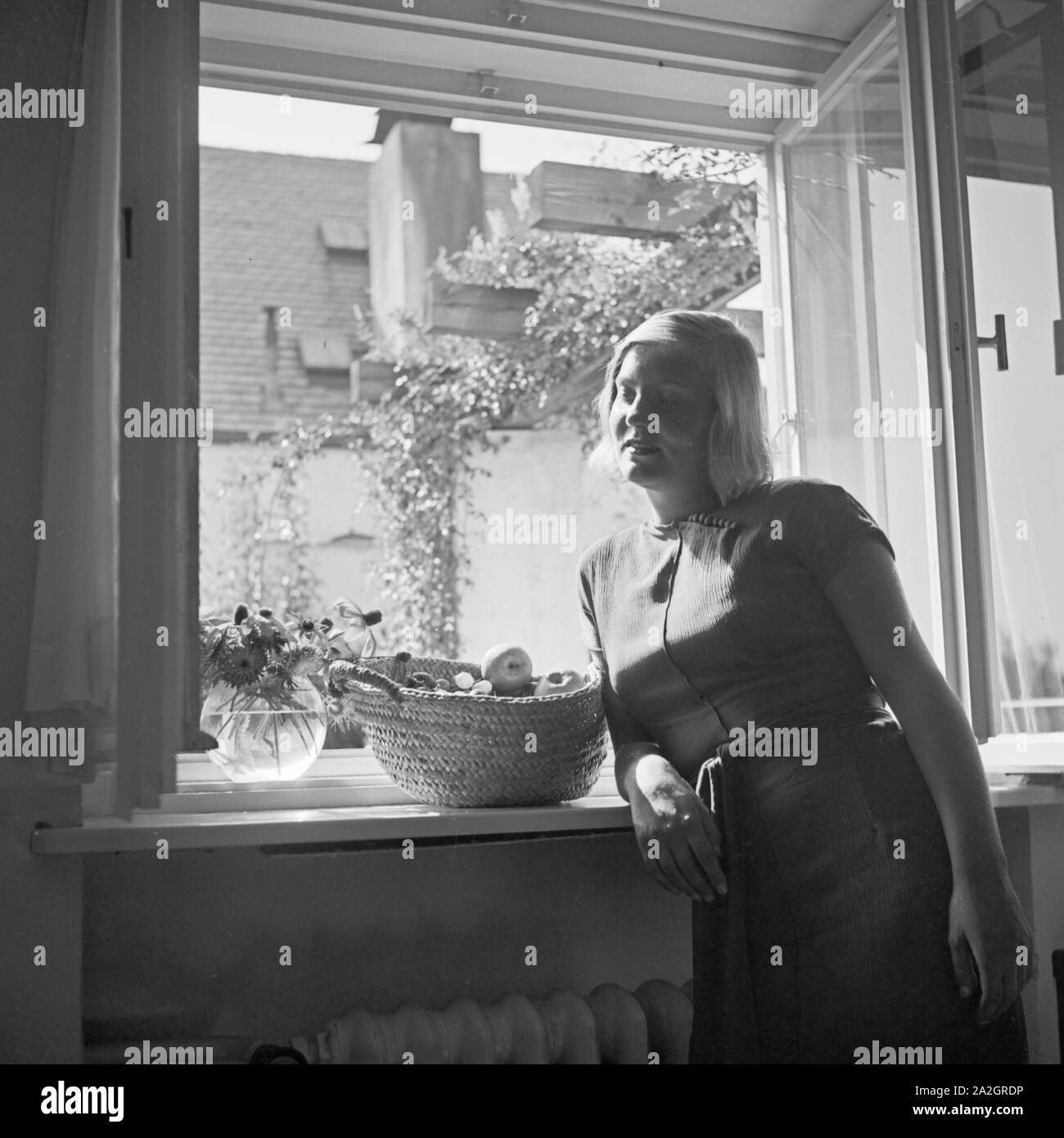 Eine junge Frau vor einem Fenster une einem Obstkorb, 1930er Jahre Deutschland. Une jeune femme à la fenêtre avec un panier de fruits, de l'Allemagne des années 1930. Banque D'Images