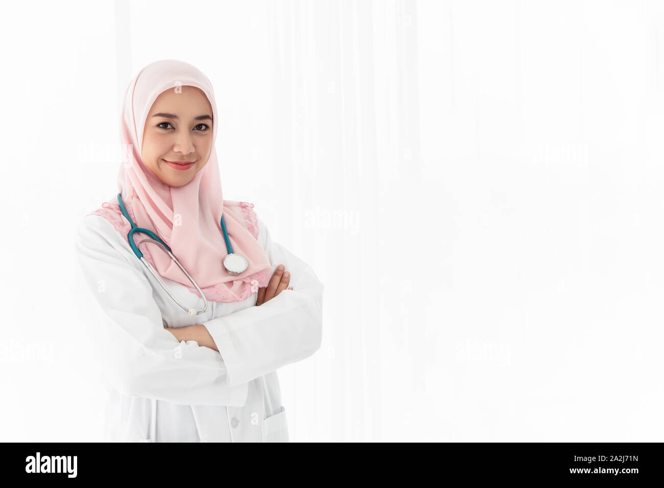 Une belle jeune femme médecin islamique avec stéthoscope se tenait dans ses bras et sourit avec confiance dans la salle d'examen près de la fenêtre avec curt Banque D'Images