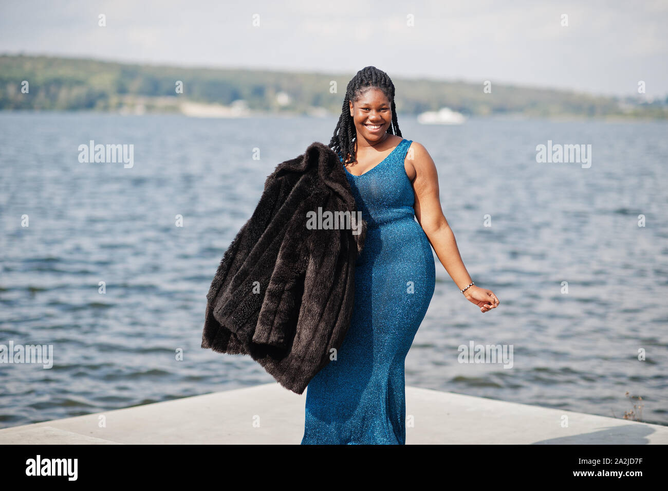 La peau foncée afro-américaine modèle taille plus posés dans une robe  brillante bleu et noir manteau de fourrure contre côté mer Photo Stock -  Alamy