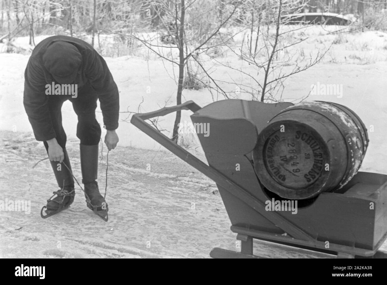 Schnallt Schlittschuhkufen sich ein Mann, une um mit dem Schlitten ein Fass Pils Schultheiss zu transportieren im Spreewald, Deutschland 1930 er Jahre. Mettre un homme sur son patin porteur à Spreewalad zone afin de transporter le baril de bière Schultheiss, Allemagne 1930. Banque D'Images