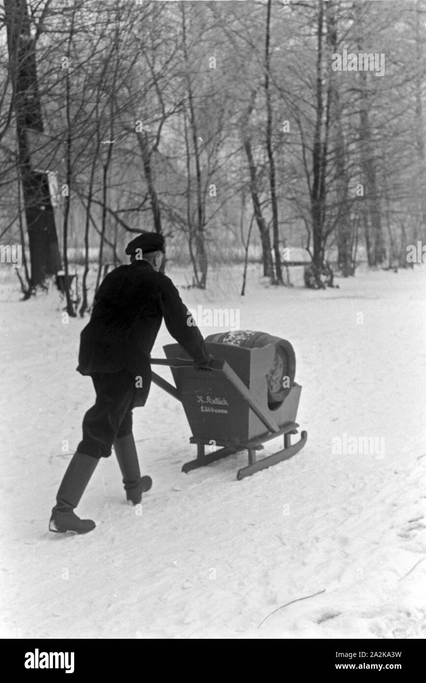Ein Mann ein transportiert Fass Pilsener Schultheiss Schlitten auf einem durch den winterlichen Spreewald, Deutschland 1930 er Jahre. Un homme transportant un baril de bière Schultheiss sur un traîneau à travers une forêt d'hiver dans la région de Spreewald, Allemagne 1930. Banque D'Images